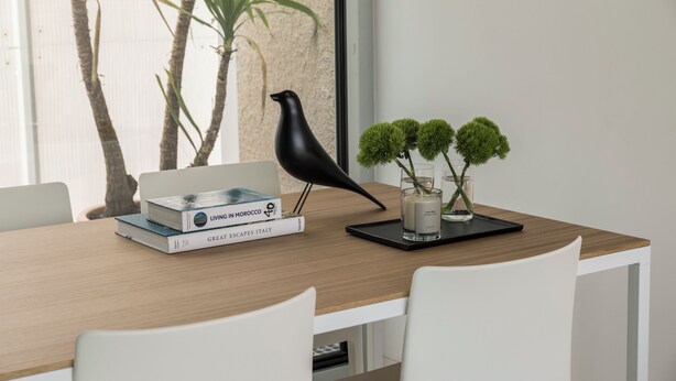 A wooden table with books, a black bird sculpture, and a small plant. - Edmond Vibes Avenida de América (Madrid)