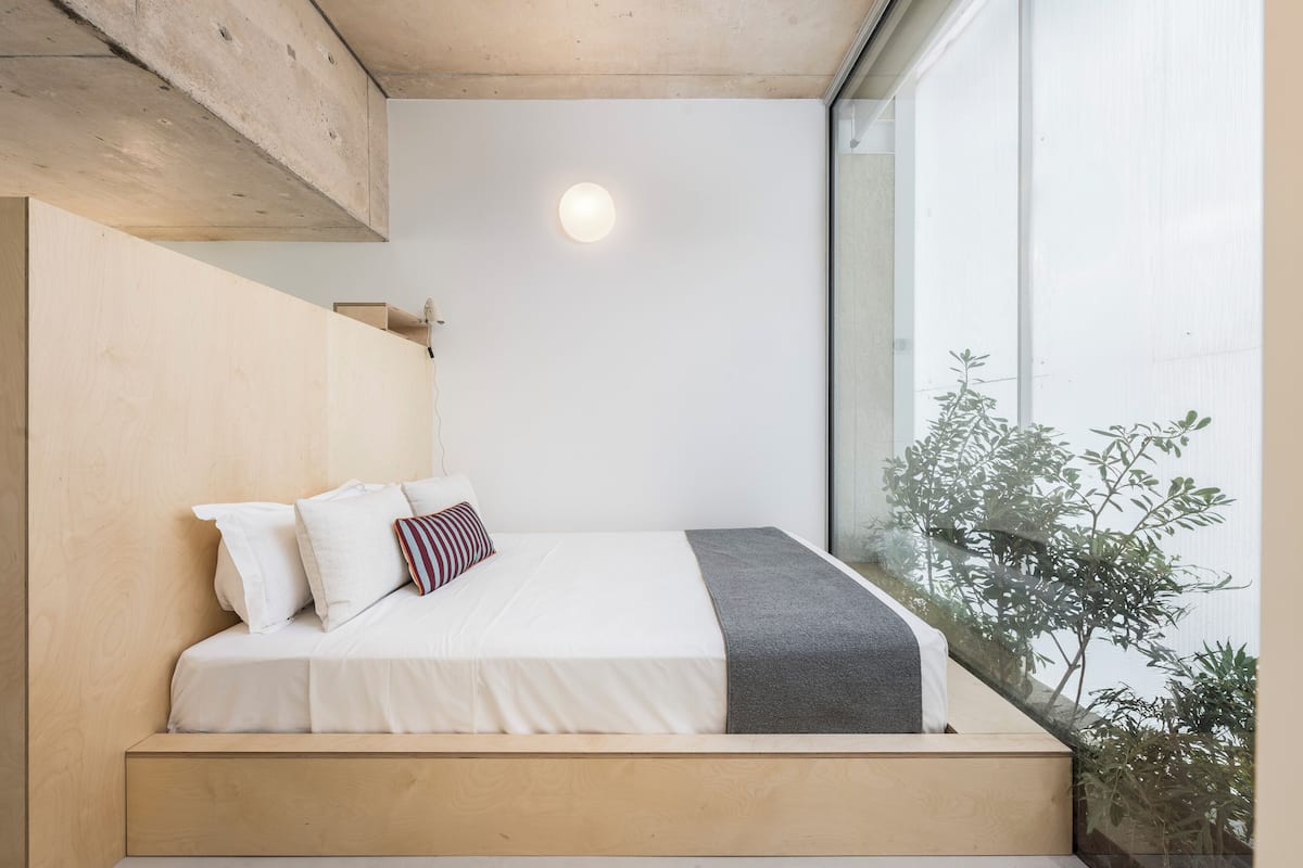 A bedroom with a wooden headboard, a bed with white bedding, a gray throw, and a bedside lamp.