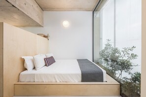 Une chambre à coucher avec une tête de lit en bois, un lit recouvert d’une literie blanche, un plaid gris et une lampe de chevet.