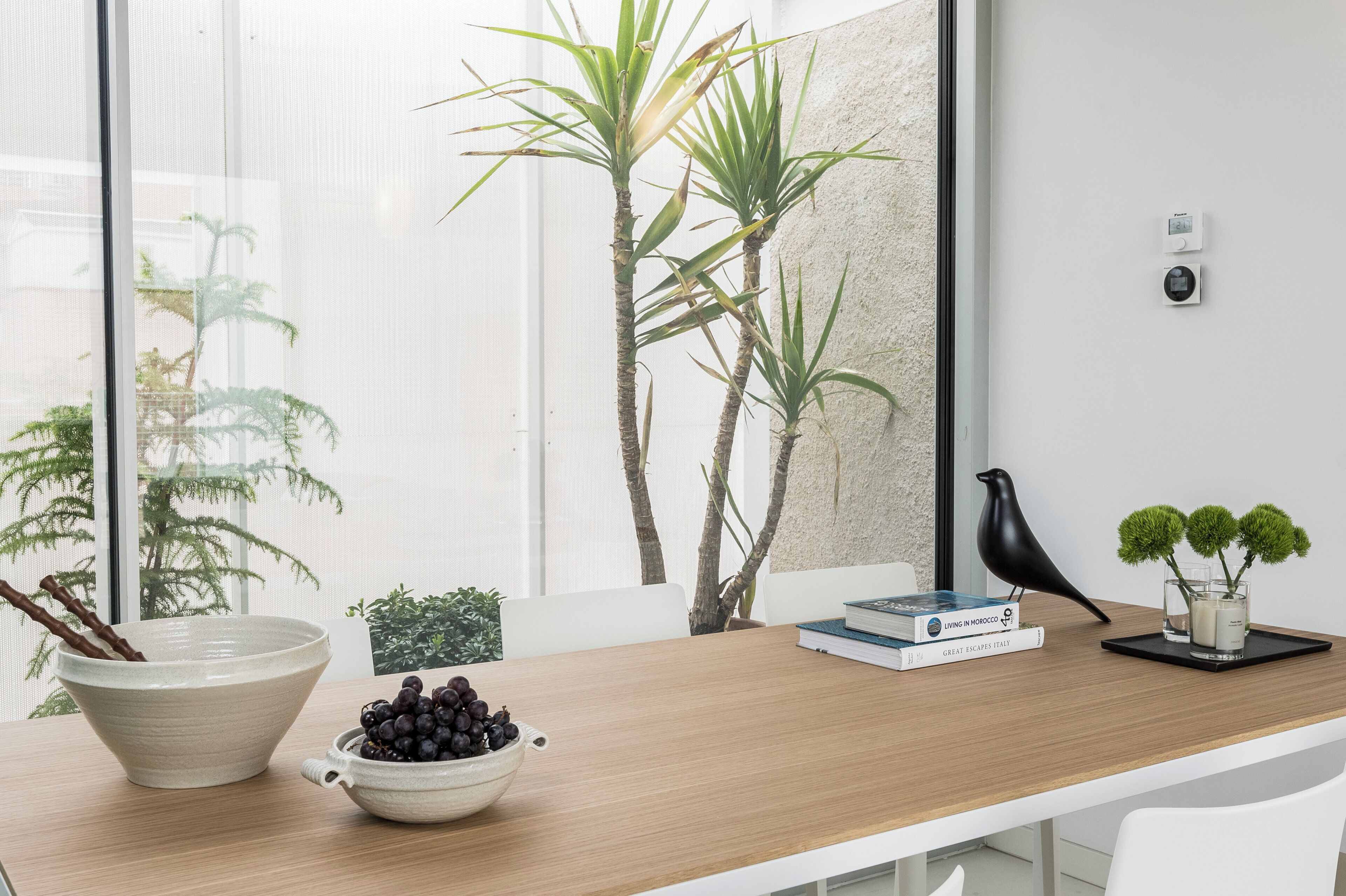 Una habitación moderna con un escritorio de madera, un cuenco de uvas, una figurita de pájaro, un libro y una planta en maceta.
