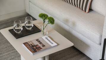 Una mesa blanca con dos vasos de agua, un jarrón pequeño con flores verdes y una revista titulada 'Openhouse'.