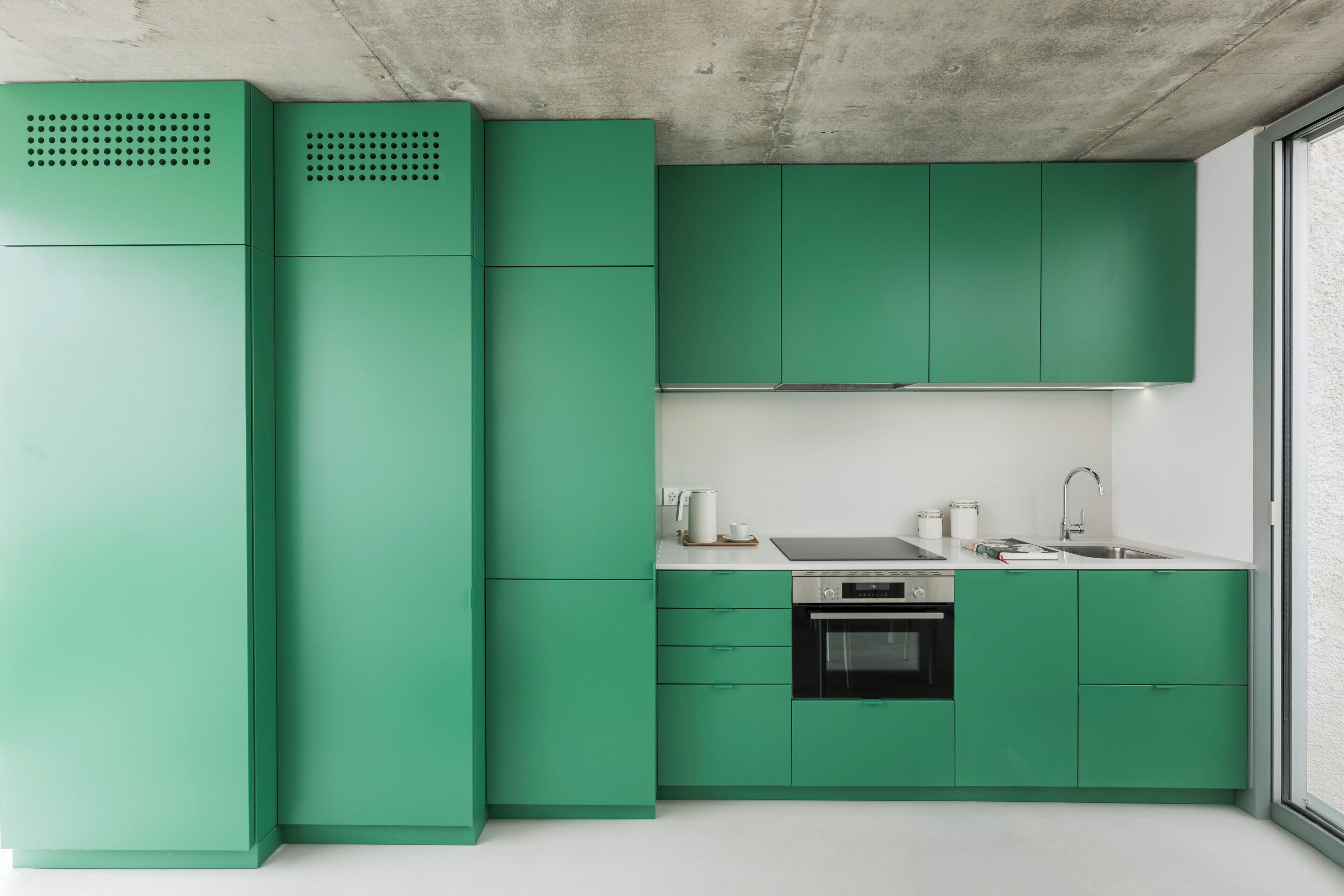 Una cocina moderna con armarios verdes, un lavamanos de acero inoxidable y un horno empotrado.