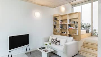 A modern living room with a flat-screen TV, a white sofa, a coffee table, and a wooden bookshelf.