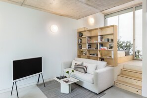 A modern living room with a flat-screen TV, a white sofa, a coffee table, and a wooden bookshelf. - Edmond Vibes Avenida de América (Madrid)