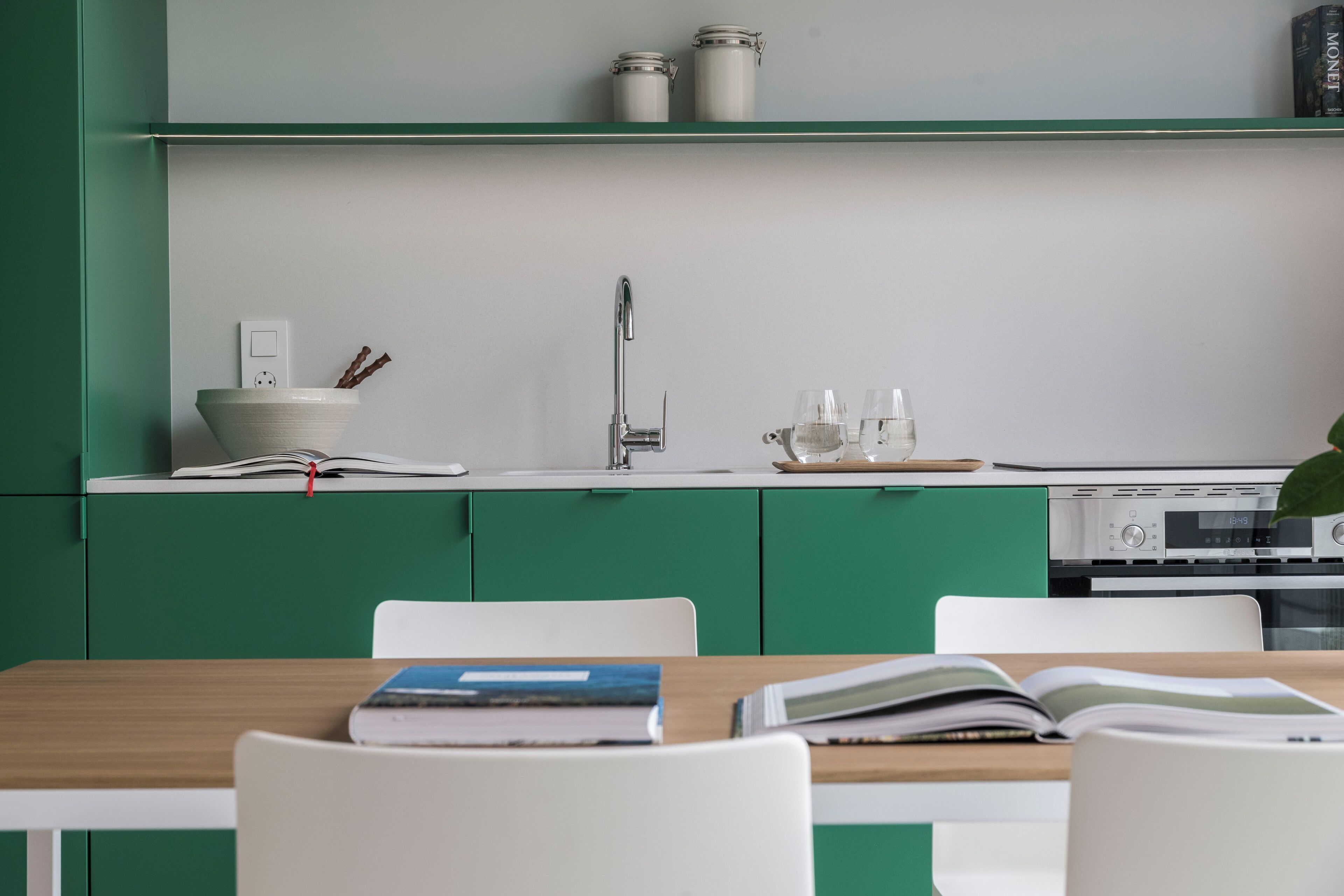 Una cocina moderna con armarios verdes, encimera blanca, un fregadero y una zona de comedor con mesa y sillas.