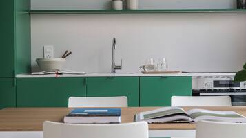 Una cocina moderna con armarios verdes, encimera blanca, un fregadero y una zona de comedor con mesa y sillas.