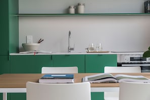 A modern kitchen with green cabinets, a white countertop, a sink, and a dining area with a table and chairs.