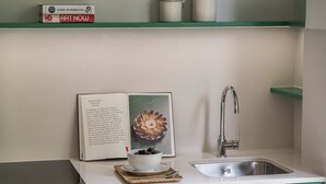 A kitchen with a white countertop, green cabinets, a stainless steel sink, a bowl of berries, and a book titled 'ART NOW' on the shelf. - Edmond Vibes Avenida de América (Madrid)
