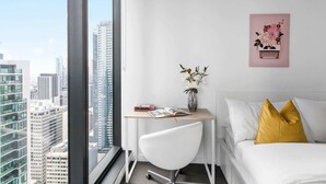 A modern hotel room with a city view, a desk with a vase of flowers, and a bed with a yellow pillow. - Pet-friendly 2BR Near Southern Cross, City Views (Melbourne)