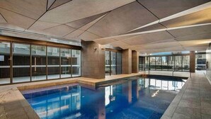 A modern indoor swimming pool with clear glass walls and a geometric ceiling design. - Pet-friendly 2BR Near Southern Cross, City Views (Melbourne)