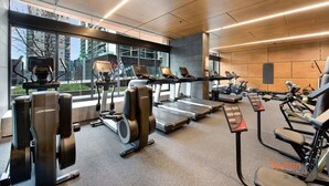 A modern gym with various cardio machines, large windows, and a view of the city. - Pet-friendly 2BR Near Southern Cross, City Views (Melbourne)