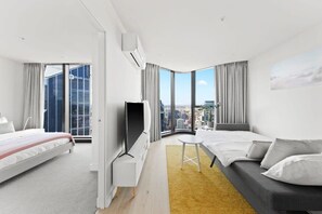 A modern hotel room with a bed, a sofa, a TV, and a large window offering a city view. - A 3BR Apt Next to Melbourne Central, Free Parking (Melbourne)