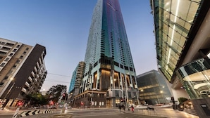 A modern high-rise building with a prominent glass facade, surrounded by other urban structures. - A Cozy Apt, Only a 5-min Walk to Victoria Market (Melbourne)