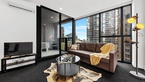 A modern living room with a large window, a sofa, a coffee table, and a TV. - A Cozy Apt, Only a 5-min Walk to Victoria Market (Melbourne)