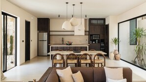 A modern kitchen with a dining area, a sofa, and large windows. - Pala House by Alfred in Bali (Pecatu)