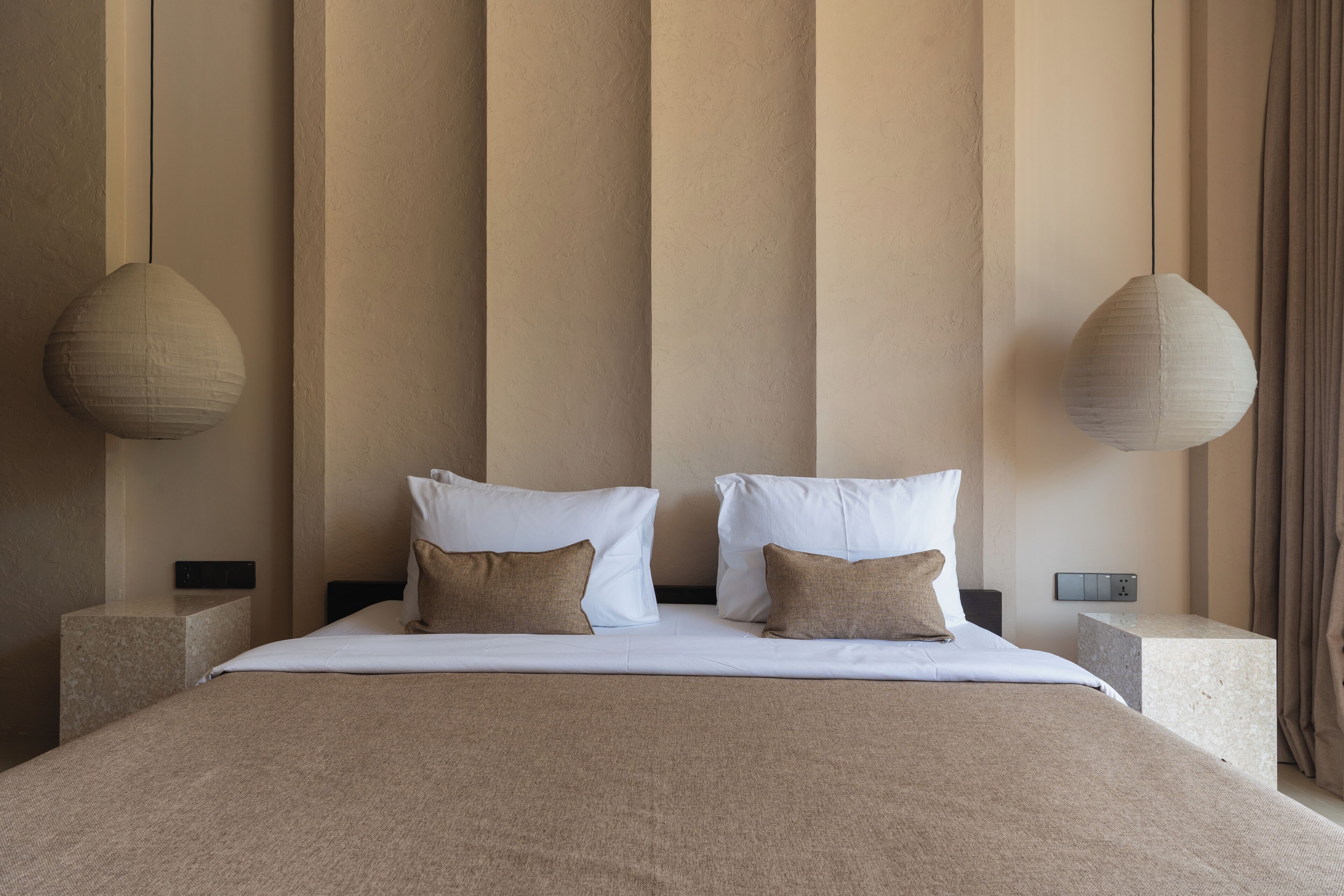 Un lit bien fait, avec une literie blanche et beige, deux oreillers et deux lampes suspendues.