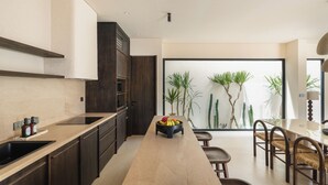 A modern kitchen with dark wood cabinets, a beige countertop, and a central island with fruit. - Pala House by Alfred in Bali (Pecatu)
