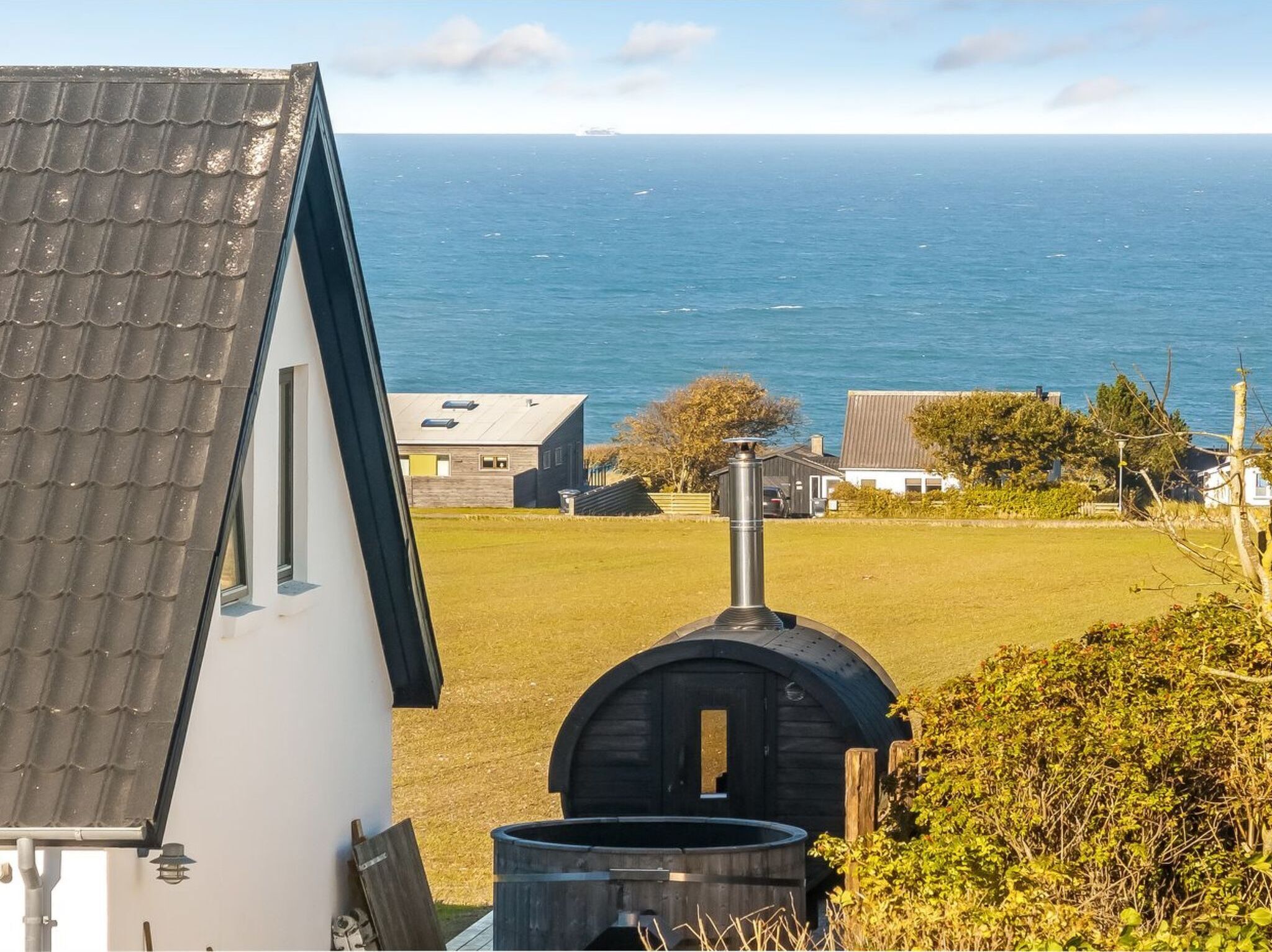 A coastal property with a view of the sea, a wooden barrel, and a small building with a sloped roof.
