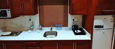Una cocina compacta con armarios de madera, un lavamanos de acero inoxidable, un microondas y un refrigerador.