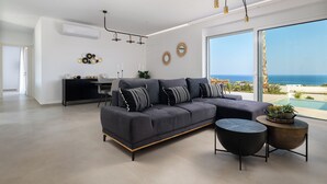 A modern living room with a grey sectional sofa, a round coffee table, and a view of the sea through large windows.
