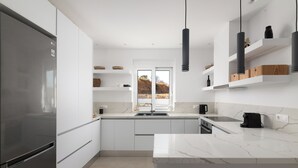 A modern kitchen with white cabinetry, a stainless steel refrigerator, a marble countertop, and pendant lighting.
