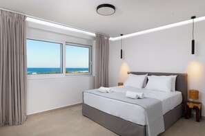 Een moderne hotelkamer met een groot bed, twee nachtkastjes, uitzicht op zee en een plafondlamp.