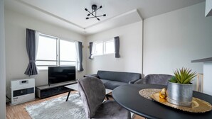 A modern living room with a grey sofa, a round dining table, and a flat-screen TV. - ANAX NORD 403 (Sapporo)