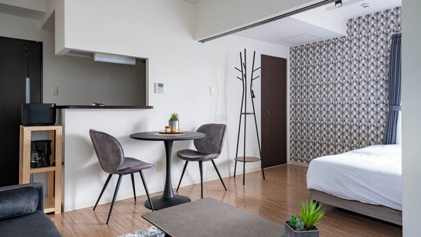 A modern hotel room with a bed, a TV, a dining area with chairs, a coffee machine, and a plant. - ANAX NORD 403 (Sapporo)