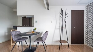 A modern dining area with a round table, two chairs, a small plant, and a coat rack. - ANAX NORD 403 (Sapporo)