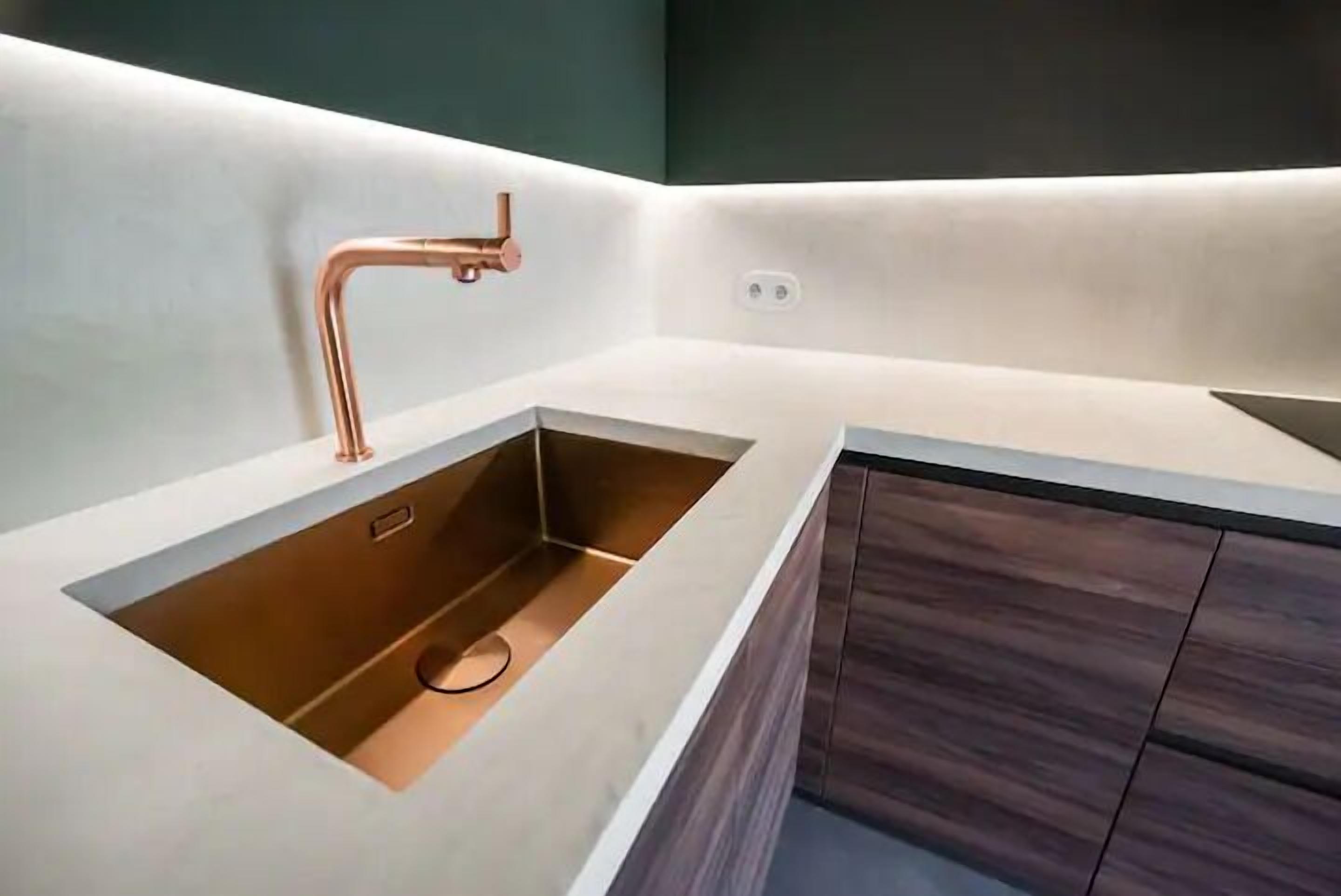 Una cocina moderna con un grifo de cobre, un lavabo integrado y armarios de madera oscura.