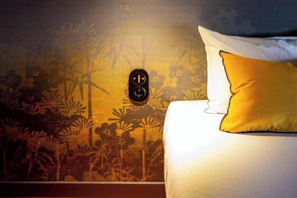 A bedroom with a bed, a wall-mounted light fixture, and a mural of a forest scene.
