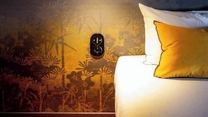 Un dormitorio con una cama, un aplique en la pared y un mural con un paisaje boscoso.