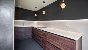 Una cocina moderna con encimera blanca, armarios de madera e iluminación colgante.