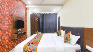 Une chambre d’hôtel avec un mur en briques, un téléviseur à écran plat fixé au mur, un lit avec une literie blanche et des oreillers colorés, et une tête de lit en bois.