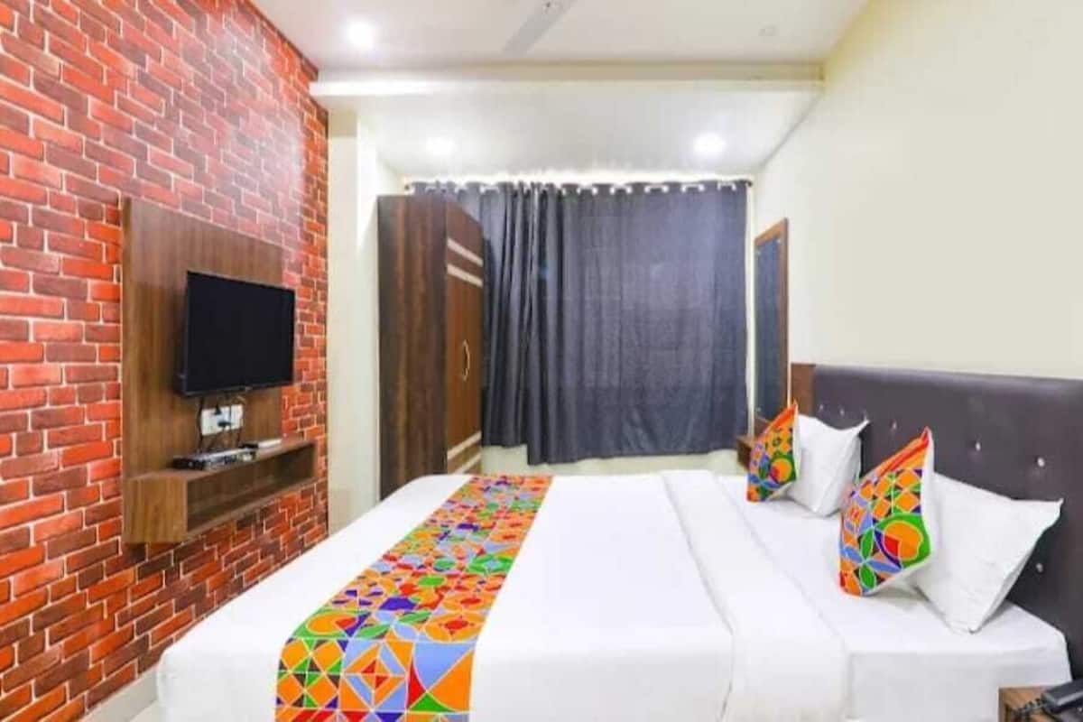 A hotel room with a brick wall, a flat-screen TV mounted on it, a bed with white bedding and colorful pillows, and a wooden headboard.