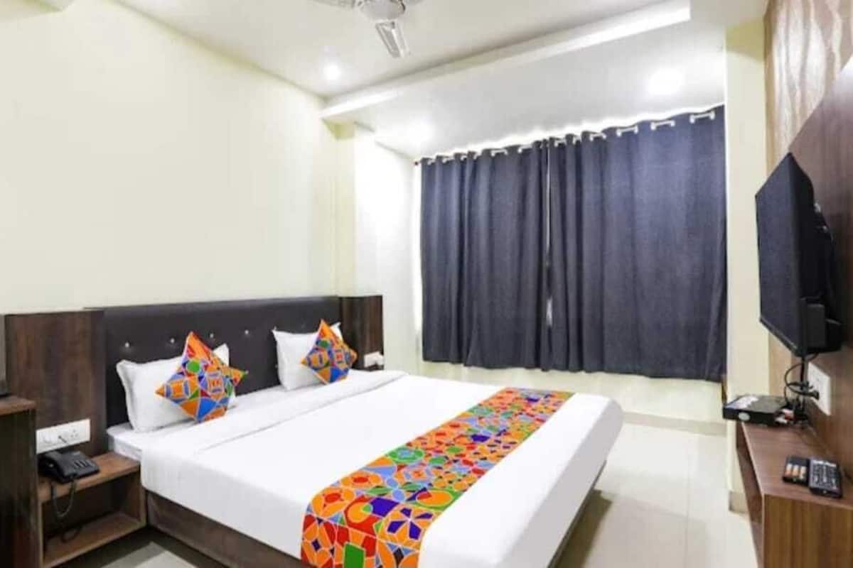 A hotel room with a bed, a desk, a chair, a TV, and a window with curtains.
