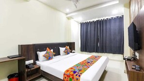 A hotel room with a bed, a desk, a chair, a TV, and a window with curtains. - The Kumar inn (Danapur)
