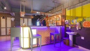 Un espace bar comprenant un comptoir, des tabourets de bar et une étagère où sont rangées les bouteilles.