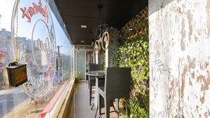Un balcon avec des meubles en osier, une vue sur la ville et un mur dont la peinture s’écaille.