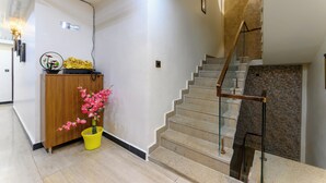 A modern interior with a staircase, a wooden cabinet, and a potted plant. - Prince Diamond Hotel (Varanasi)