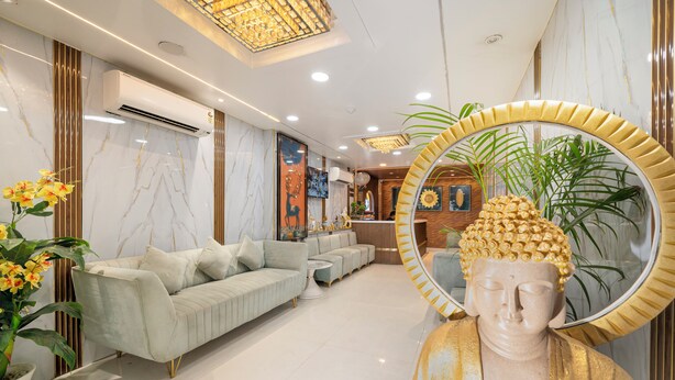 A modern living room with a sofa, a round mirror, and a Buddha statue. - Prince Diamond Hotel (Varanasi)