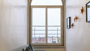 A corner room with a green sofa, a large arched window, and a tiled floor. - Prince Diamond Hotel (Varanasi)