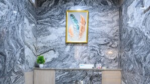 A bathroom with a marble wall, a framed artwork, a toilet, and a shower area. - Prince Diamond Hotel (Varanasi)