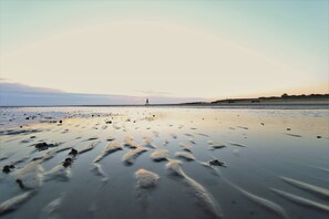 A beach with a lighthouse in the distance, calm water, and footprints in the sand. - Holiday Home 'Olenbrook' with Shared Terrace, Shared Garden and Wi-Fi (Cuxhaven)