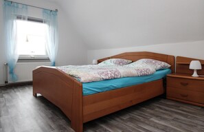 Een slaapkamer met een houten bed, een nachtkastje met een lamp en een raam met gordijnen.