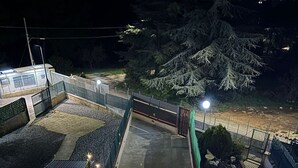 Una terraza en la azotea con suelo de madera, una reja metálica y vistas a árboles y un edificio al fondo.