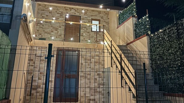 Un edificio de dos plantas con balcón, escaleras y entrada protegida por una reja.