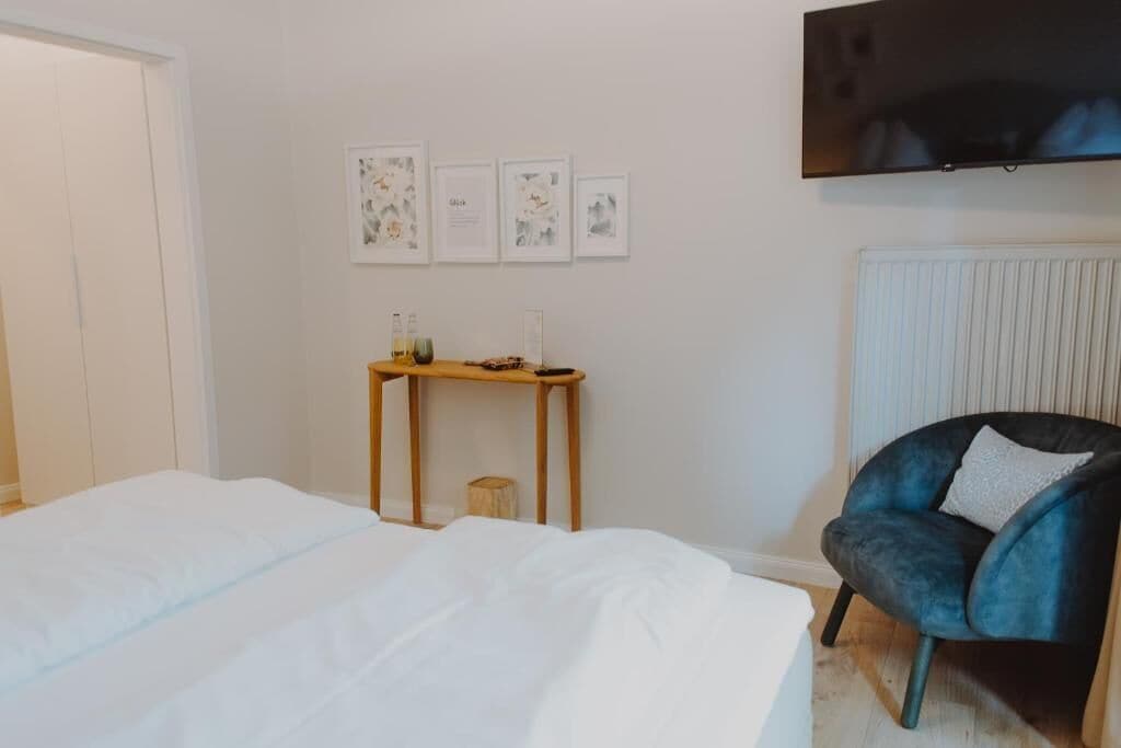 Een slaapkamer met een bed, een klein houten tafeltje, een stoel en een aan de muur bevestigde televisie.
