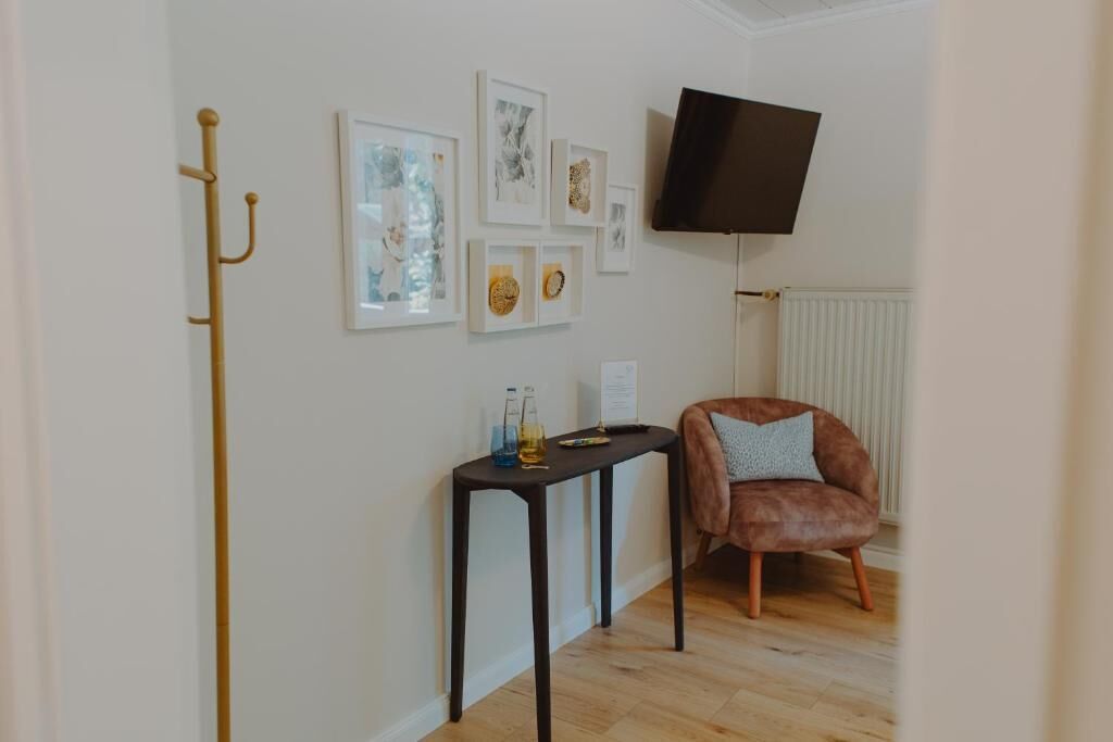 Ein Zimmer mit Holzboden, einem braunen Ledersessel, einem kleinen Tisch mit Flasche und Fernbedienung sowie einem an der Wand befestigten Fernseher.
