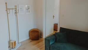 A room with a green sofa, a tall floor lamp, a round ottoman, and a mirror on the wall. - Haggn&Co (Neukirchen)